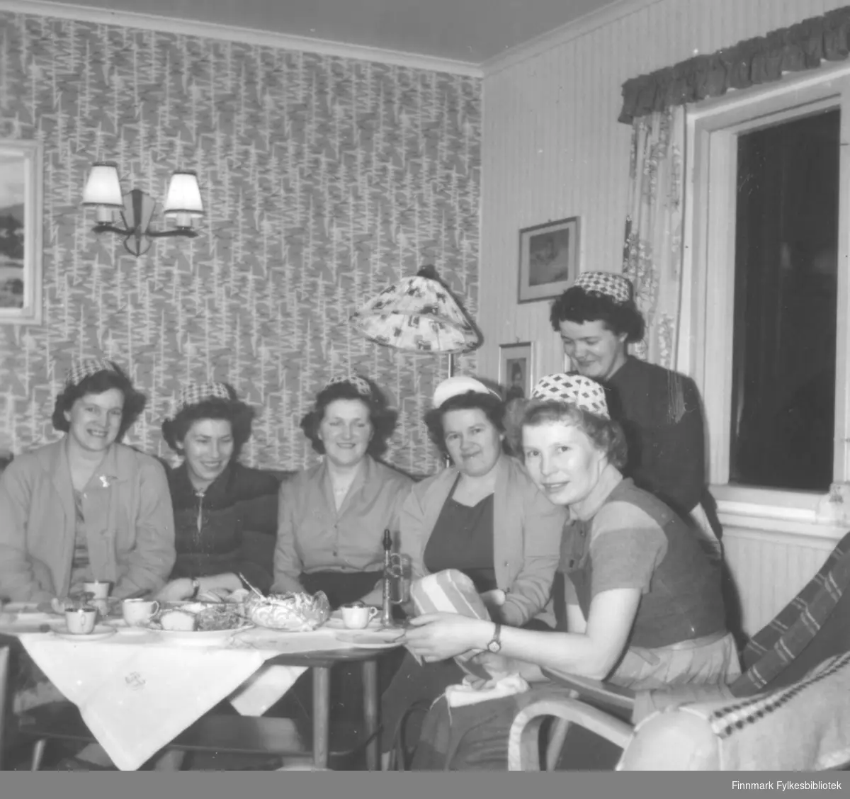 Syforening i Fosseveien 3, ca. 1960-1965. Bildet ser ut til å være tatt på samme foreningsmøte som 06046-014, men her har alle medlemmene tatt på seg hatter med lik fasong. Det står et instrument på bordet