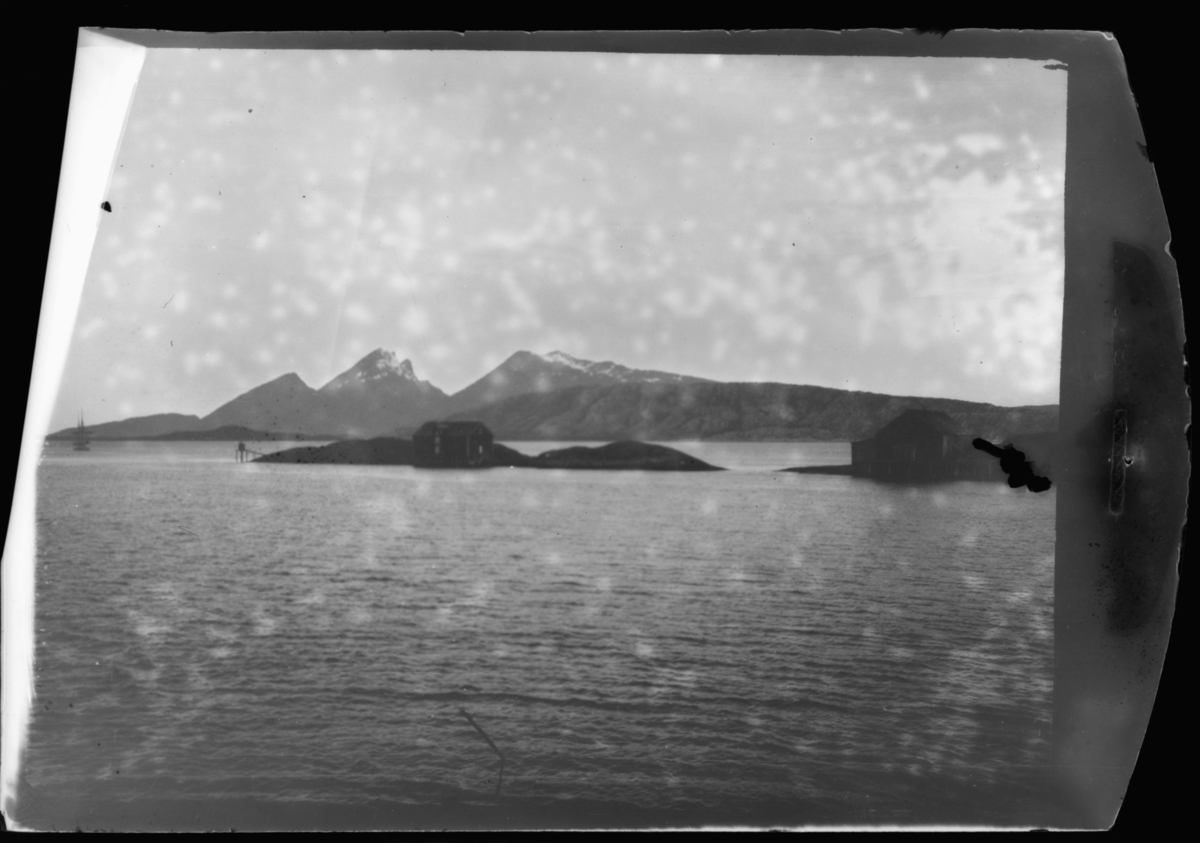 Bildet er tatt fra et skip / hurtigrute mot fastland. Mitt på bildet ligg en øy, det står et stabbur på øya. Høye fjell på bakgrunn.