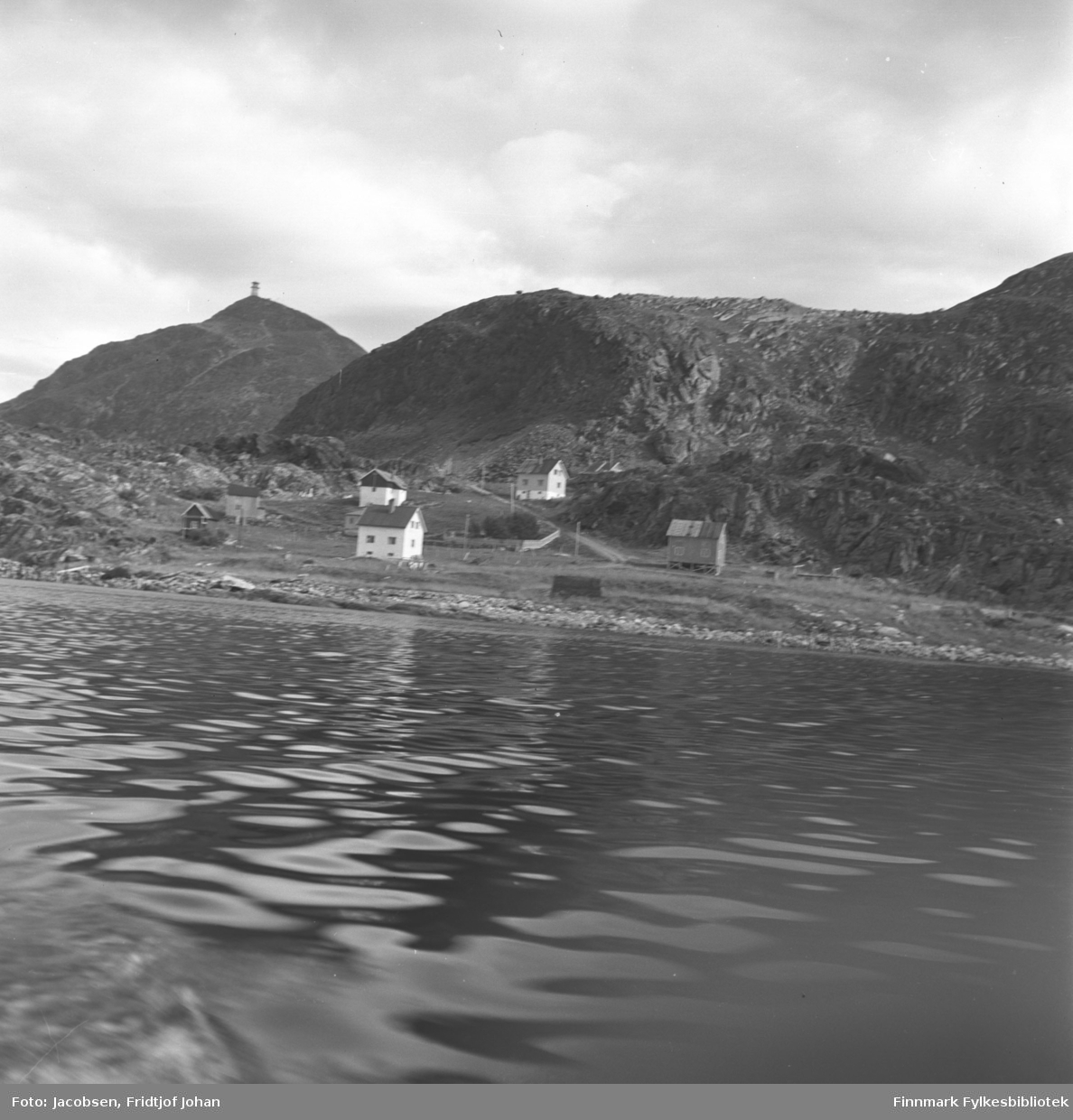 Bildet er tatt fra en båt mot Leirvika som ligger rett vest for Rypefjord. Fem boliger og et naust står på området. Veien fra Leivikhøgda/Rv 94 ses midt på bildet. Fjellet Tyven med masta under bygging ligger til venstre på bildet. Sjøen er blikkstille og det er overskyet.