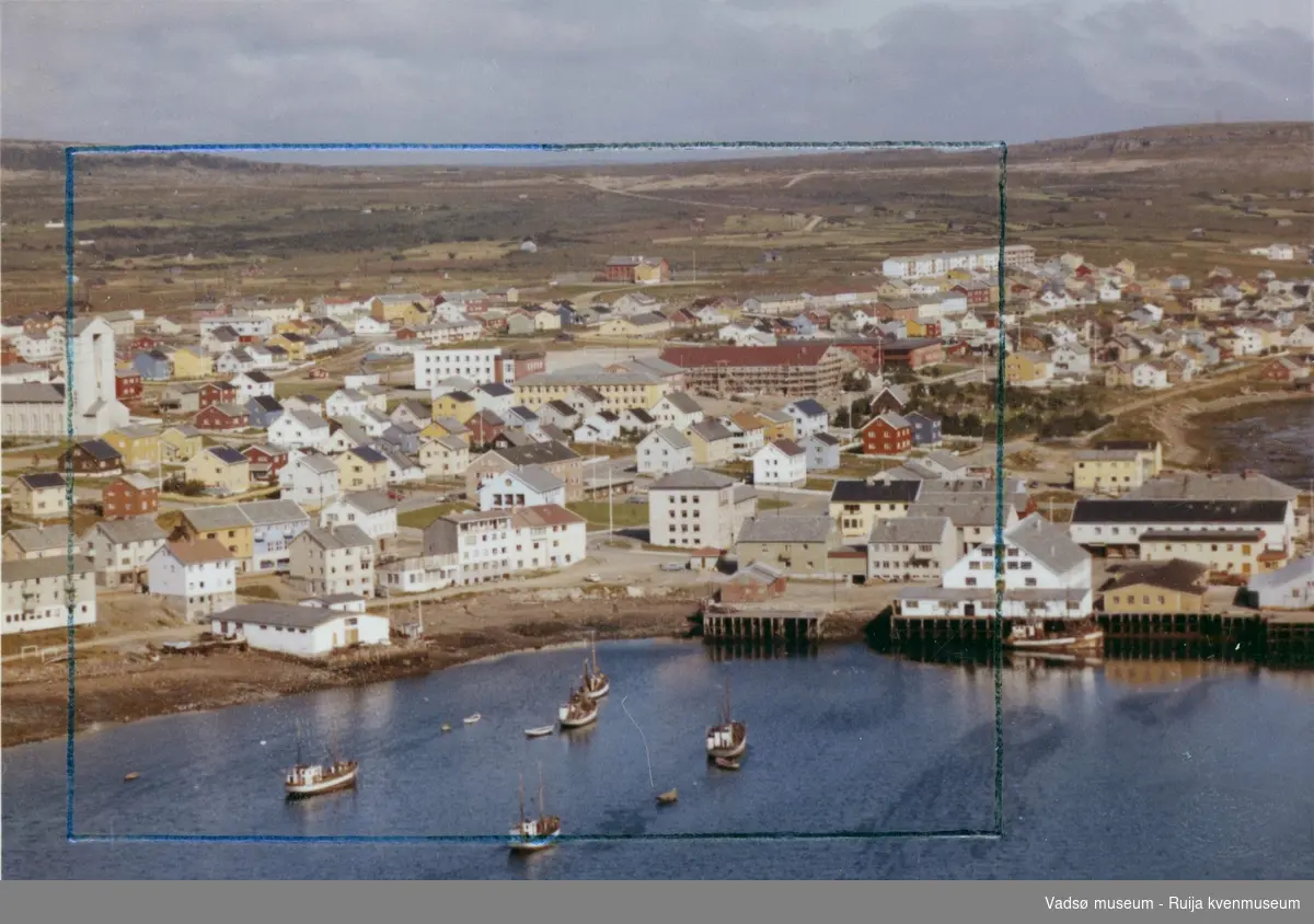 Flyfoto av Vadsø, 1963. Viser havna med kaianlegg og midtbyen. Deler av ytrebyen ses i bakgrunnen.