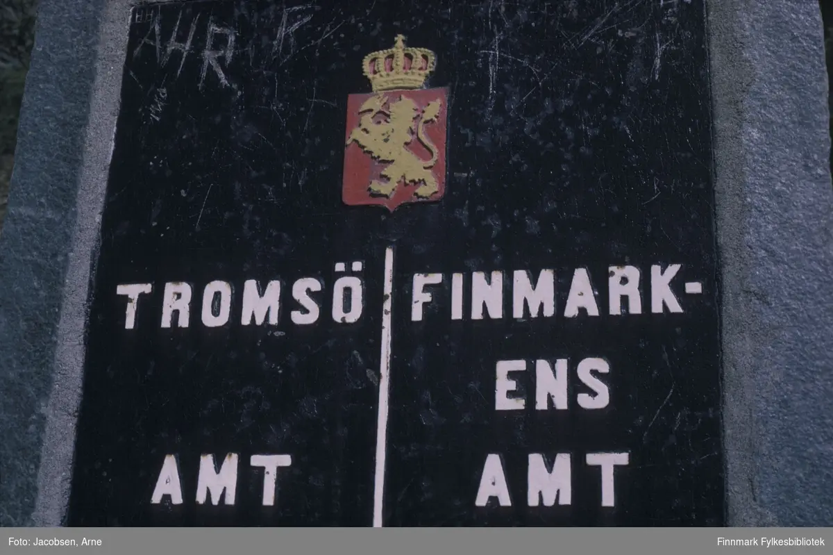 Grensesteinen mellom Troms og Finnmark fylker. En stor stein med en plate som har Norges riksvåpen øverst med delelinje med TromsÃ¶ amt på venstre side og Finmarkens amt på høyre. Litt ripete med bl.a intitialer. Steinen står langs E6 på Alteidet
