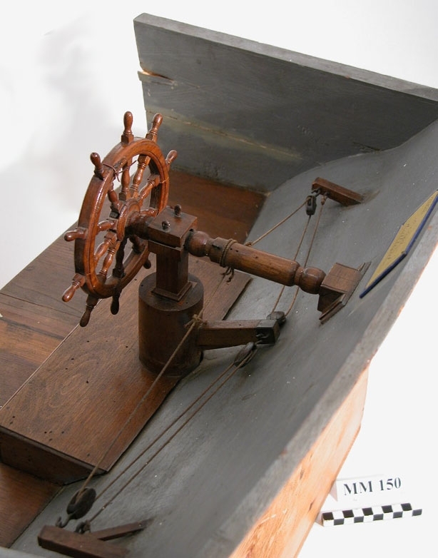 Drillhjul, beslaget. Modell av trä, fernissad. Modellen fastsatt till akterskeppet av ett fartyg, gråmålat.