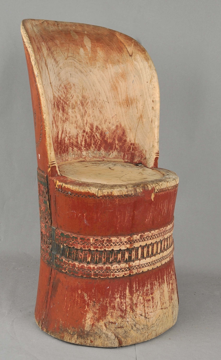 Kubbestol som er måla med raud botnfarge og med eit utskore, grønmåla band rundt nederse del av stolen. Smalt utskore felt langs kanten på setet og ryggen.