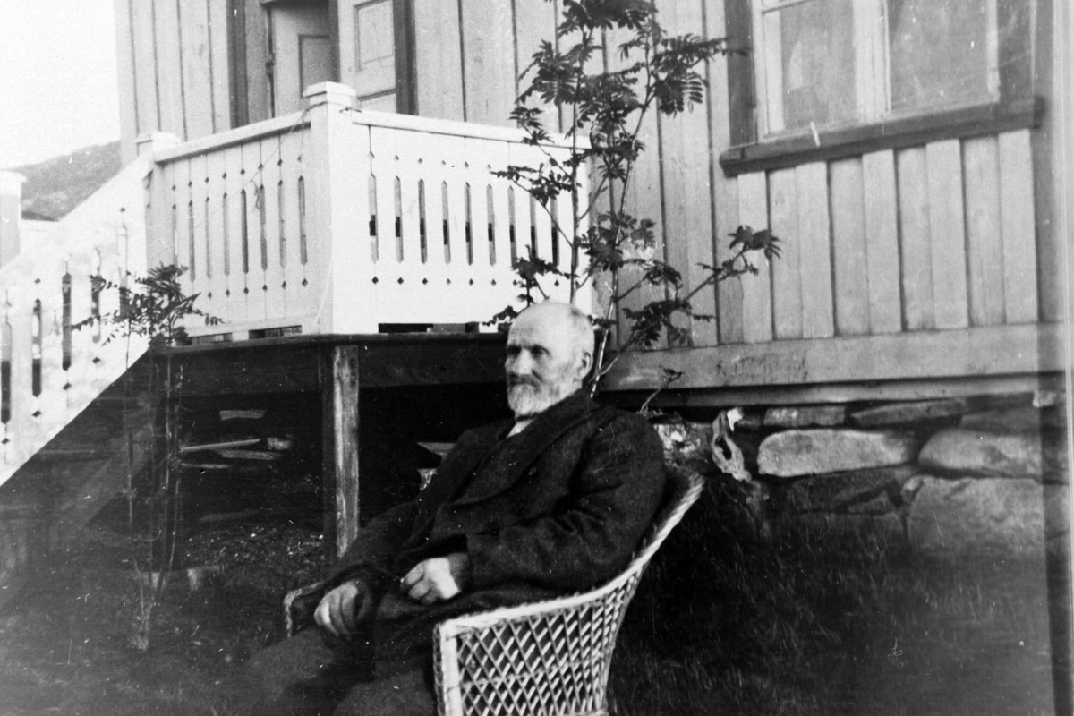 Eldre mann i en kurvstol, fotografert utendørs foran en veranda.