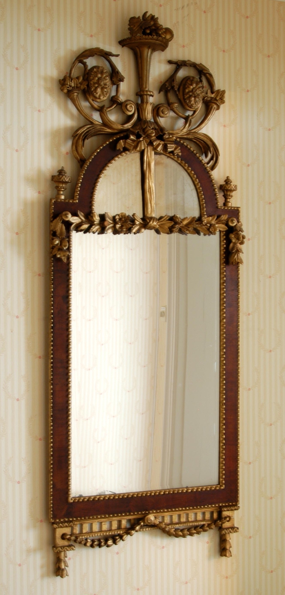 Speilets ramme er prydet med perlestaver, girlandre, sløyfe, urner og tannsnitt.