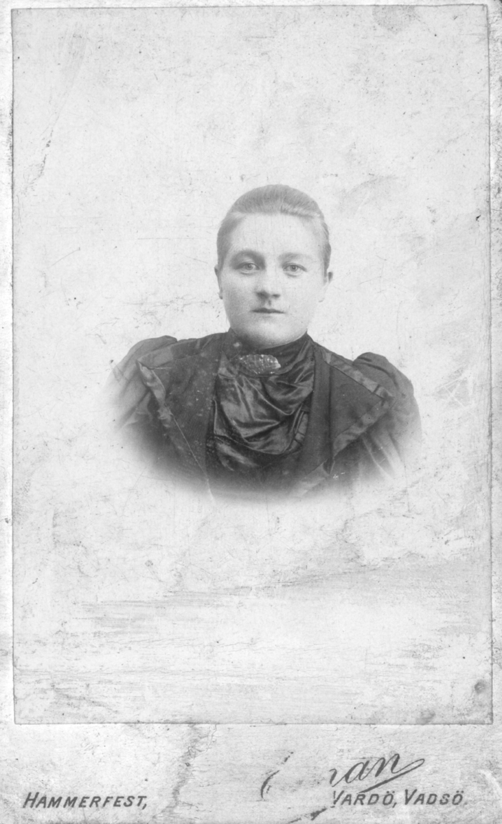 Portrett av ukjent kvinne. Hun er kledd i kjole og har en brosje rundt halsen. Bildet rolig tatt på slutten av 1800-tallet, begynnelsen av 1900-tallet.