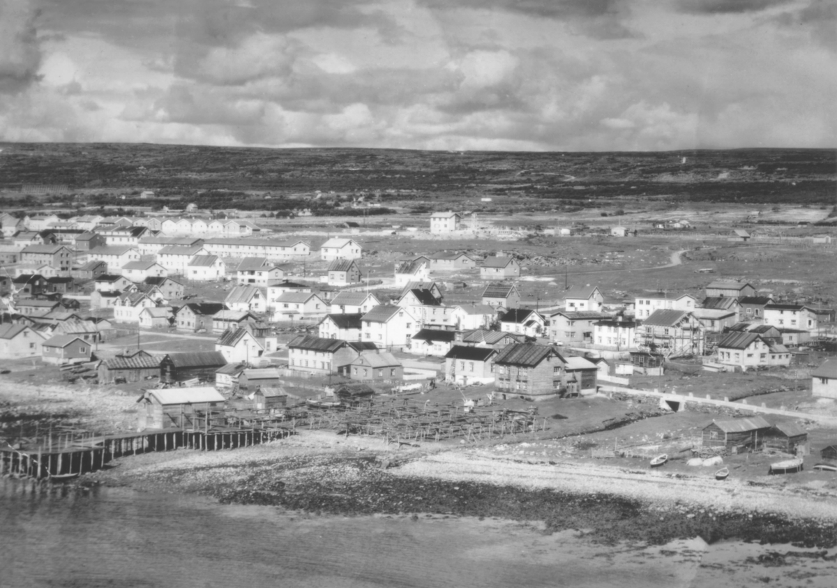 Oversiktsbilde fra Yttrebyen i Vadsø i 50-tallet. Grenreisningshusene står i rekke og rad. Bildet er tatt fra sjøen mot bebyggelsen.  Landhuselva og Hvistendalsgate i forgrunnen.