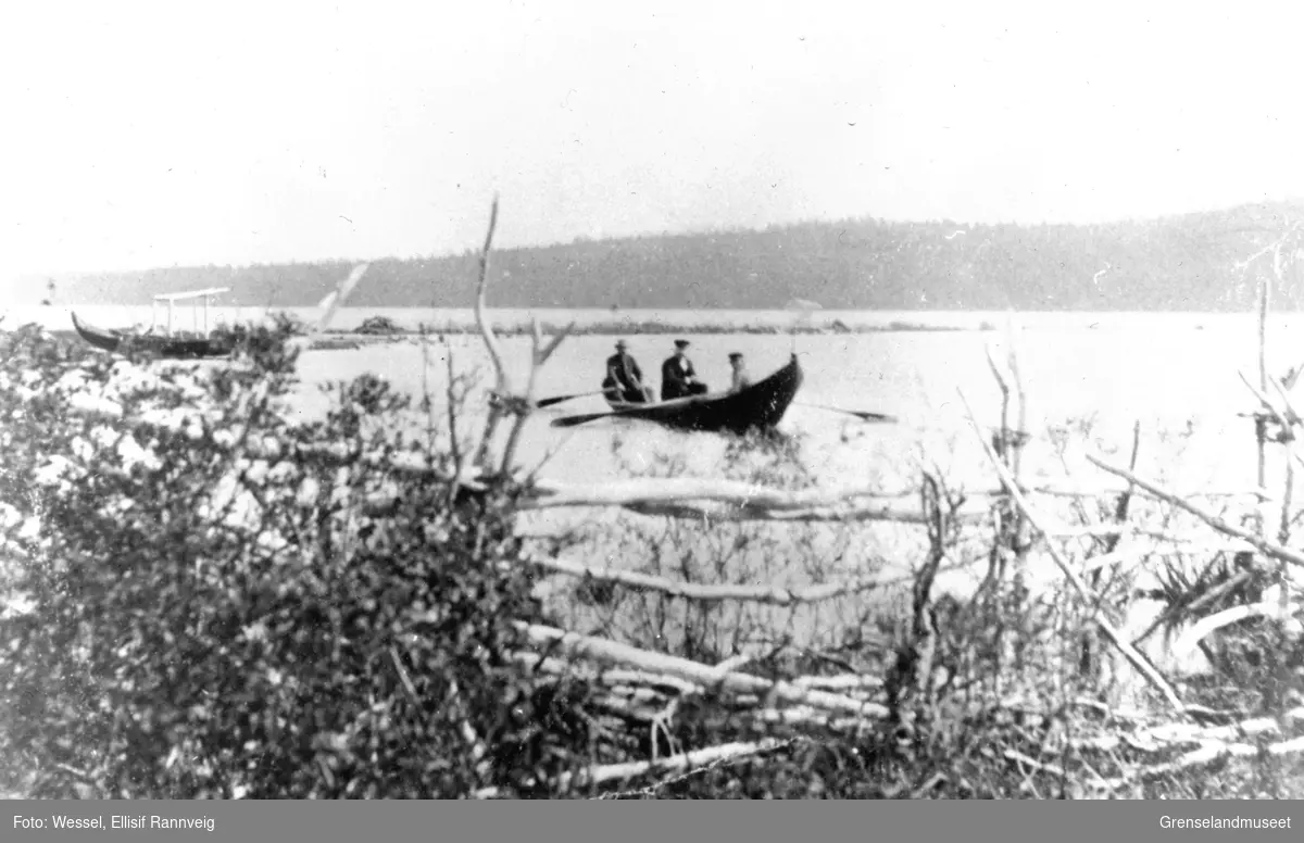 Elvebåt med tre personer på Pasvikelva, ved  Salmijärvi. Den bakerste mannen er muligens doktor A. B. Wessel.