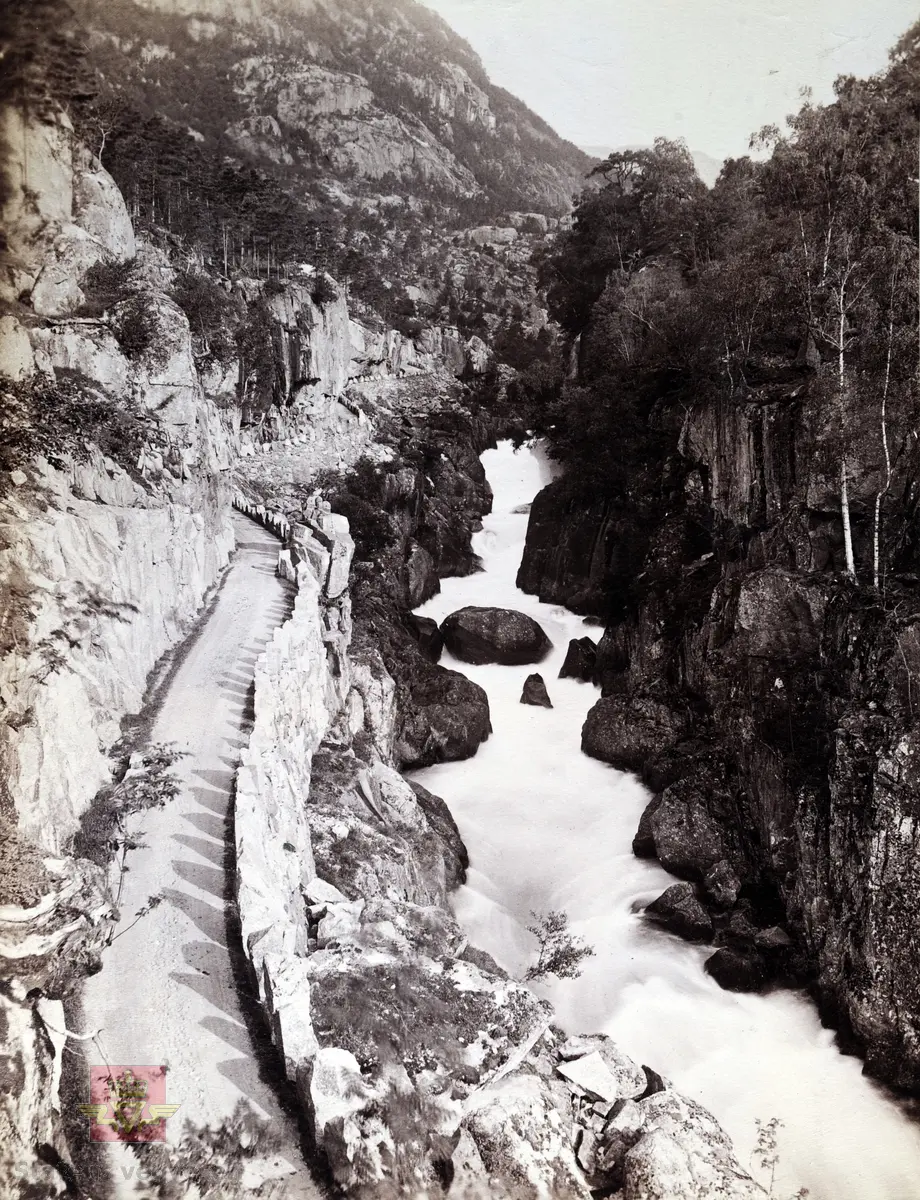 "Veianlæg". Veg gjennom Bratlandsdalen, Hordaland og Rogaland fylker. Bygget 1879 - 1888.   Vegtrasè med stabbesteinrekkverk langs elva. Ryfylke.