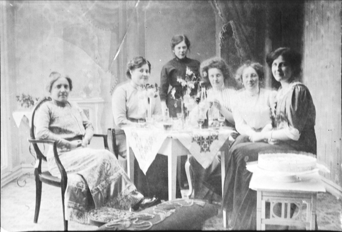 Gruppebilde av kvinner rundt et bord med glass og flaske på, tatt i Magdalene Normans studio i Harstad.