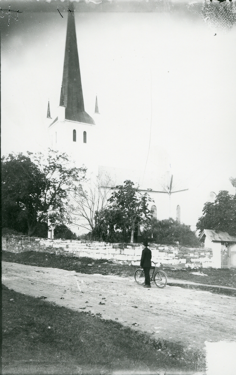 Norderhov kirke. Mann med sykkel oppstilt foran steinmuren som omgir kirka.