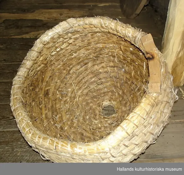 Bikupa, halm, flätad, med snidade delar av trä (ingång för bina). Kupan är rund och har en öppning på toppen.