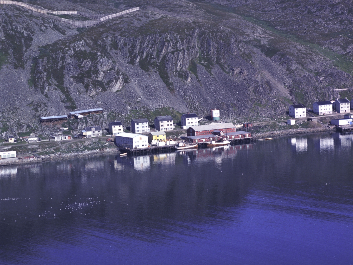 Flyfoto fra Kjøllefjord. Negativ nr. 122726. Fiskebruket midt i bildet var kjent som Aarsæther på 70-tallet, men var muligens FiNoTro tidligere? Helt til høyre på bildet sees enden av Dampskipskaia og til venstre enden av Kullkaia.