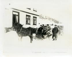 4 pelskledde menn sitter på en slede med hest foran. Bildet 