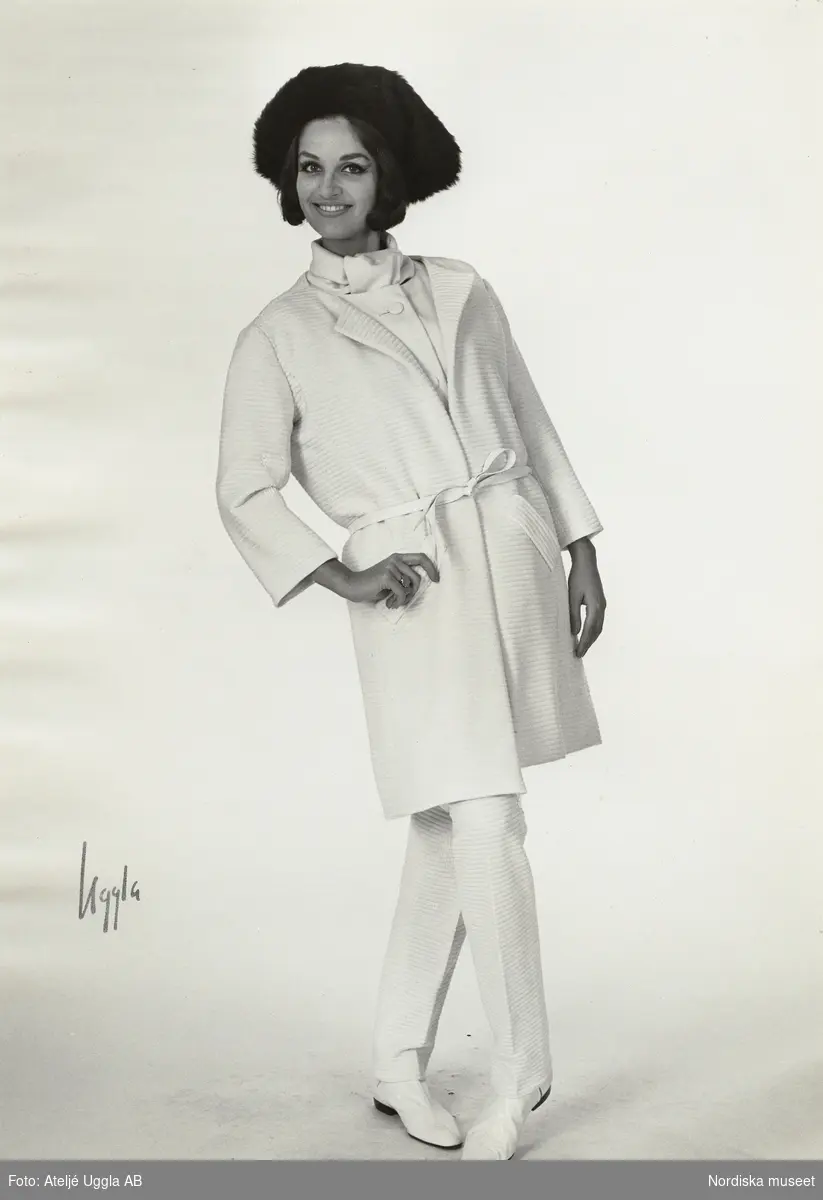Modell i kappa och byxor i vit jersey, platta skor och hatt. NK:s Franska, original från Courrèges, höst.