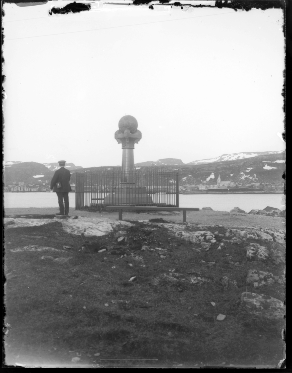Meridianstøtten på Fuglenes i Hammerfest. En mann står med ryggen til kamera og ser mot sentrum av Hammerfest