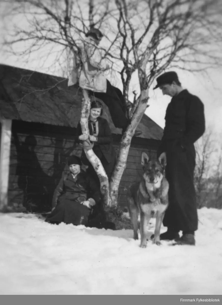 Påsken 1935. Gertrud Gunnari sittende i snøen, Solveig Evanger står ved siden av, Ella Gunnari har klatret opp i treet, Thomas Gunnari og hunden slapper av utenfor slåttehytta.