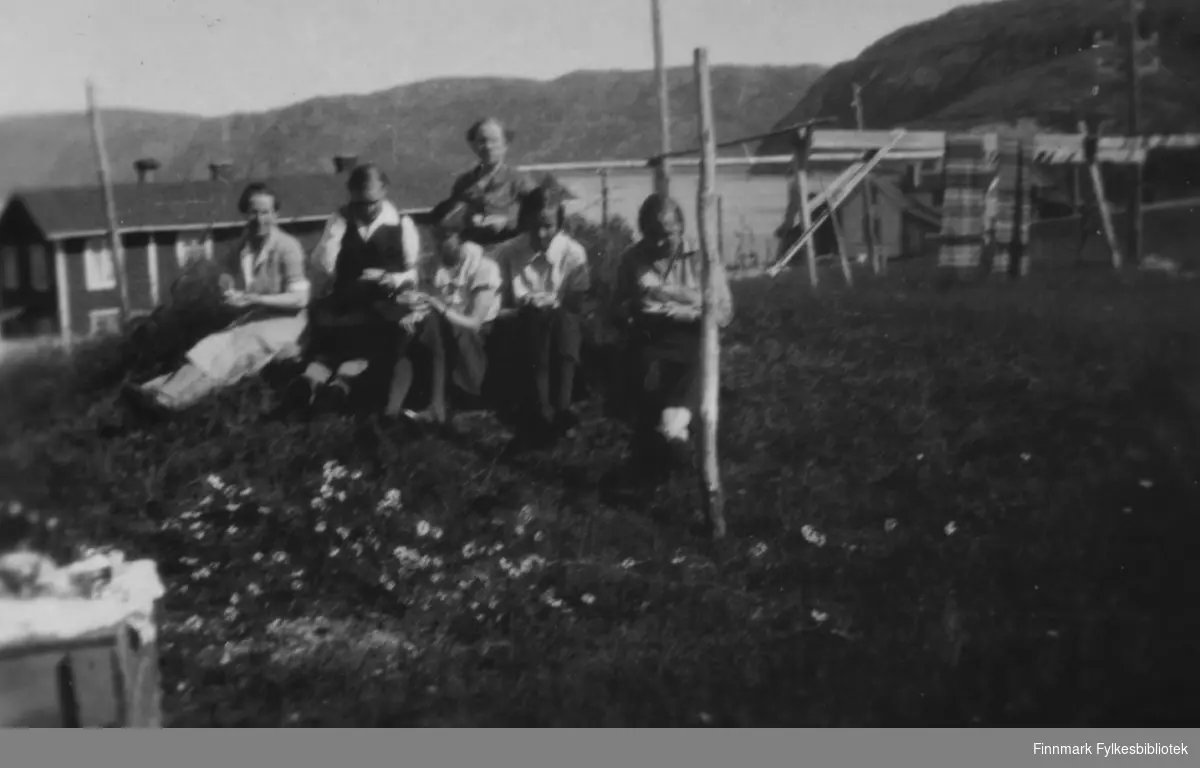 Kvinner samlet til fotografering ute i Bugøyfjord, sommeren 1934. På bildet ser vi fra venstre Aino Gunnari, Gertrud Gunnari, Solveig Evanger, Lydia Hadaja, Ruth Grønvigh og Ella Gunnari i enga ved familien Gunnaris hus.