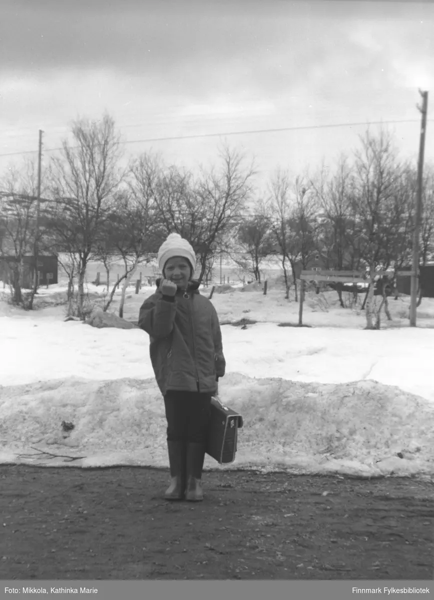 Anita Lindseth med skoleransel i veikanten i Bugøyfjord. Hun hytter med neven mot fotografen! Bildet er tatt ved samme anledning som 05007-244