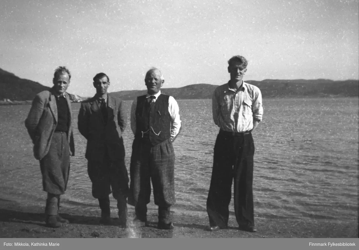 Besøk fra Finnmark jordsalgskontor, bildet er tatt i fjæra ved Mikkelsnes. Fra venstre: To menn fra jordsalgskonoret, Aksel Konrad Mikkola med vest, urkjede og kommager, Mikkel Mikkola. Bildet er tatt ved samme anledning som 05007-319