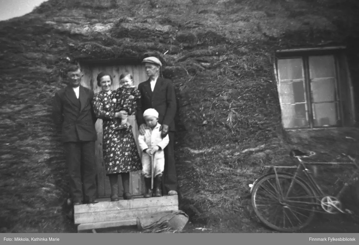Aleksander og Lembi Dørmænen med datteren Randi på armen foran familiens boliggamme i Neiden. Mannen til høyre er Olaf Jakobsen med sønnen Erik.