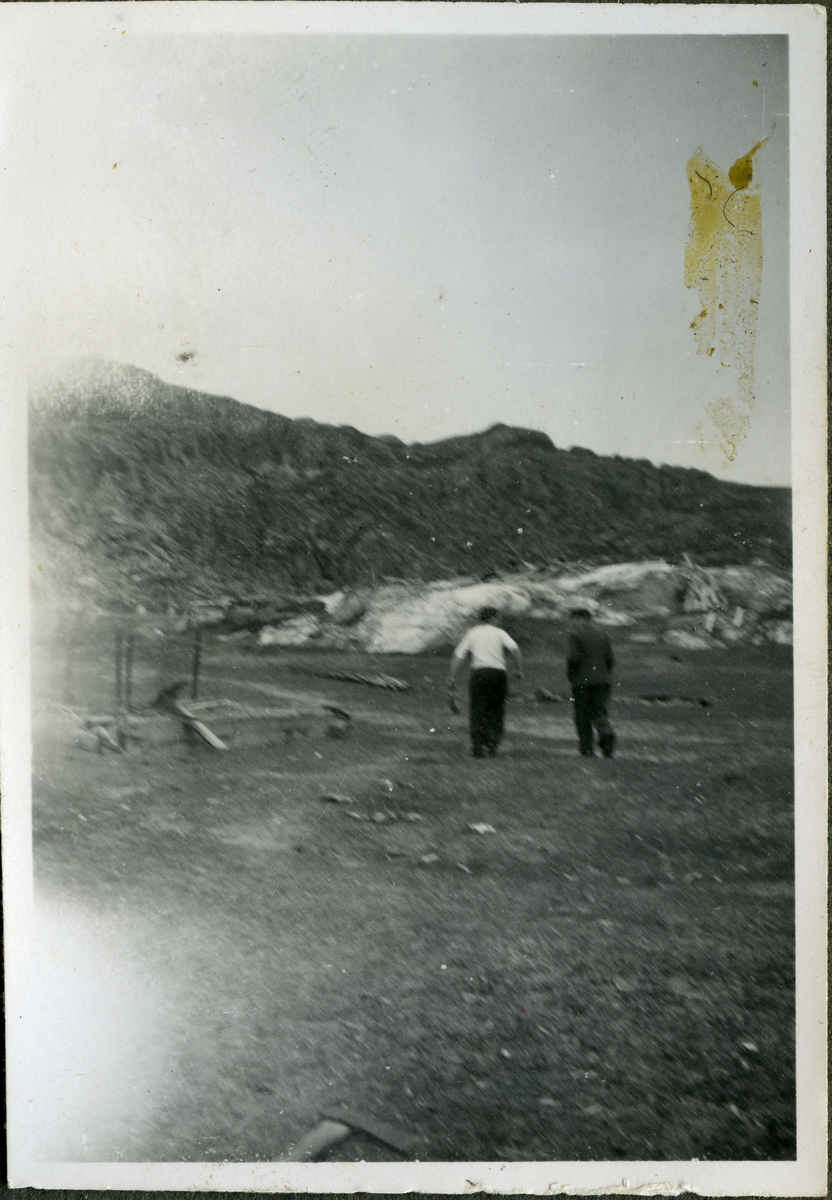 To ukjente menn går i gruvelandskapet på skiferbruddet i Friarfjord. I området kan man se steiner, redskaper og fjell. Mennene er kledd i jakke, bukse og skjorte.