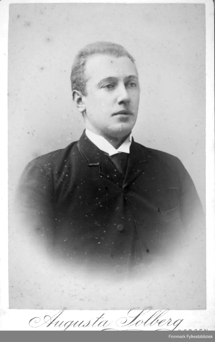 Portrett av en mann iført en mørk dress. I halsen stikker den hvite skjortekragen fram under dressjakka.
