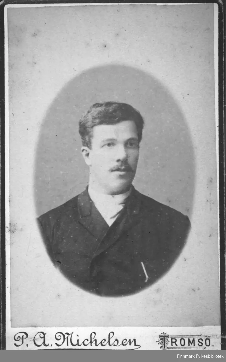 Portrett av en mann iført en mørk jakke. En lys genser eller tørkle ses rundt halsen hans.