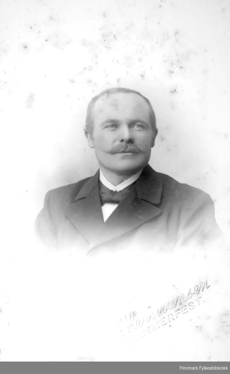 Portrett av en mann iført en mørk dressjakke, hvit skjorte og sløyfe i halsen.