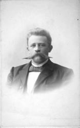 Portrett av en mann iført en mørk dressjakke og vest. Han ha