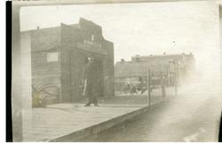 Mann som står utenfor smia/butikken sin. På skiltet står det