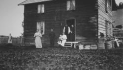 Utenfor et trehus på Elvebakken. I døråpningen står det en m