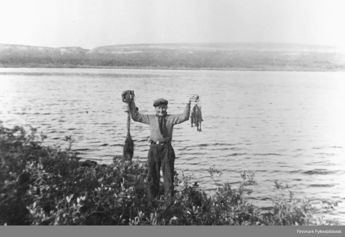 William Mietinen 14 år på fisketur i Østervann ovanfor Vestre Jakobselv. Han står ved vannet og løfter opp en bunt av fisk (ørret?). På den andre handen holder han garn. Han ser veldig fornøyd ut. Bak vannet ser vi fjellet.