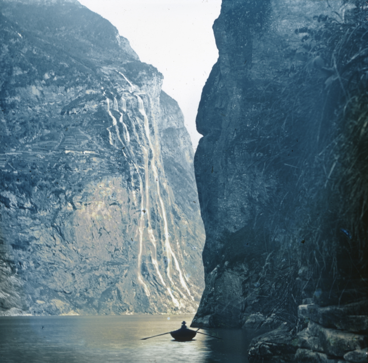 Dias. En mann i en robåt ror i Geirangerfjorden ved fossen De syv søstre.