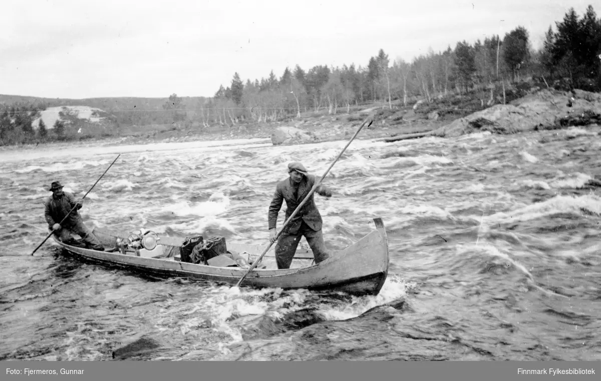 To menn staker en elvebåt. Fornavnene deres er Niilas og Àndi, sted og etternavn er ukjent, men elva er nok Karasjohka. Bildet er tatt våren 1946.