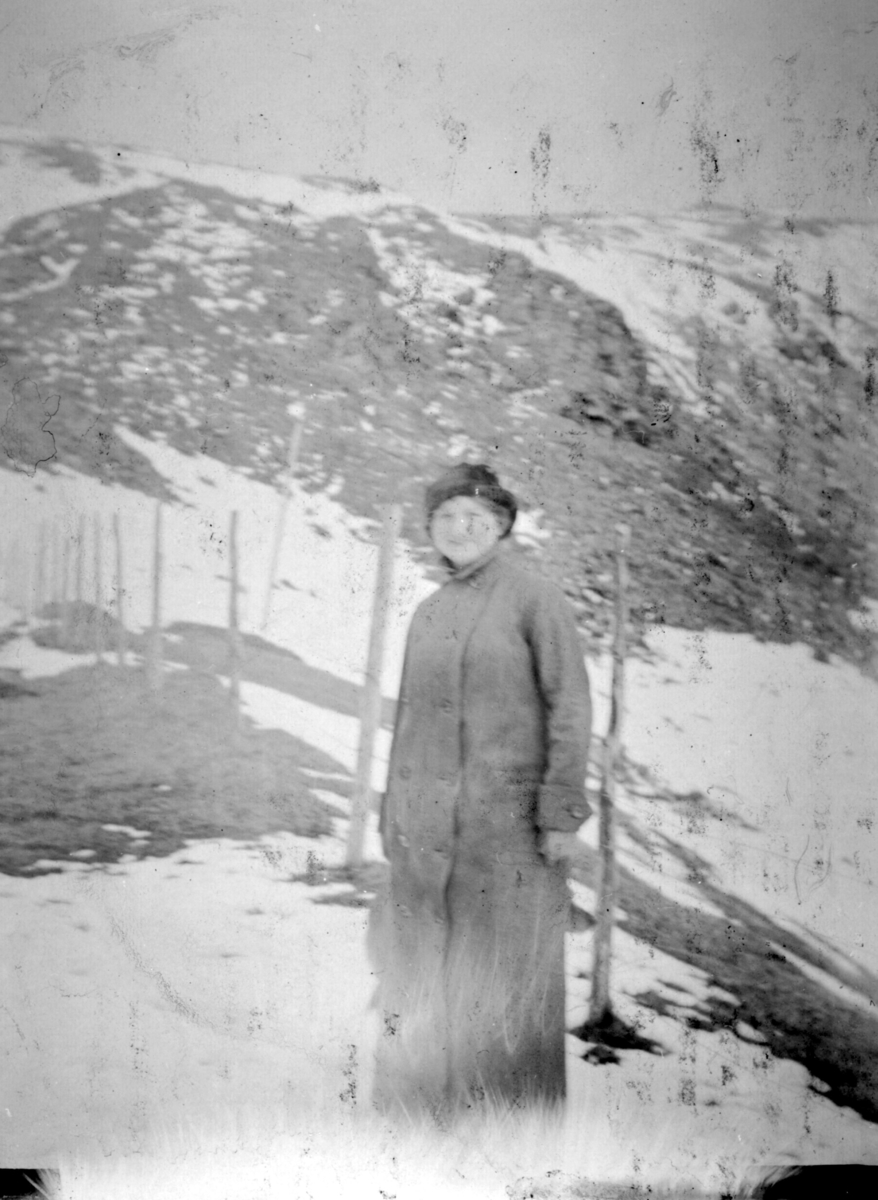 Sara Soelberg står ute kledd i kåpe og hatt. Bak henne kan man se snødekte fjell.