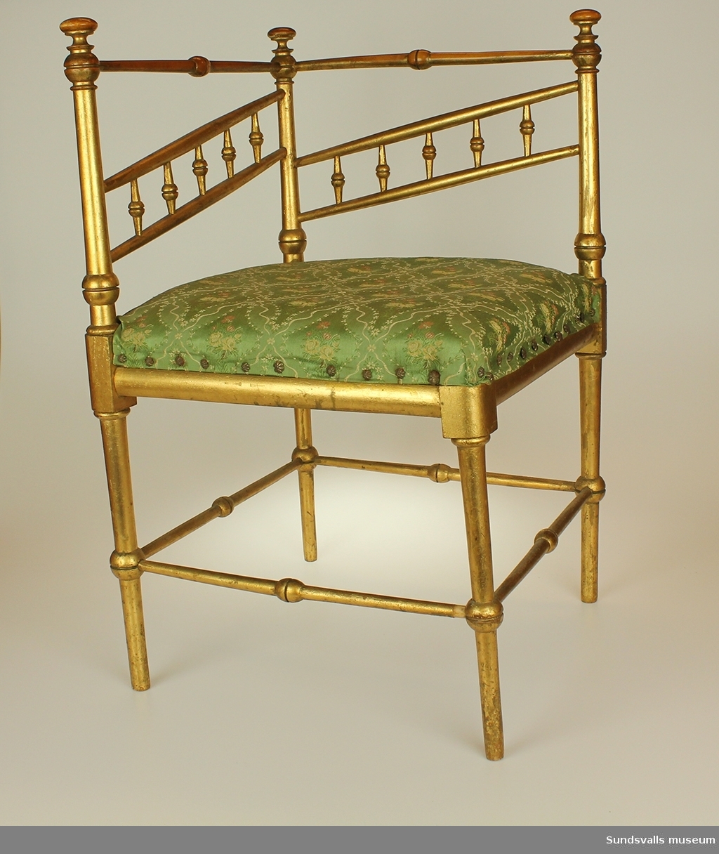 En guldkolorerad svarvad björkstol. Sits av sadelgjord och tagelfylld dyna som klätts med vit och rödblommigt grönt möbeltyg vilket fastsatts med möbelspik i form av stiliserade prästkragar. Nr 2 av ett par.