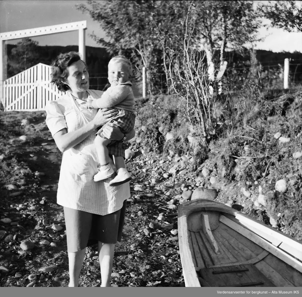 En kvinne holder et barn på armen på elvebredden.