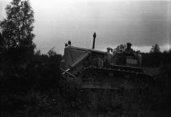 En voksen mann i en beltetraktor som brøyter vekk jord og tr