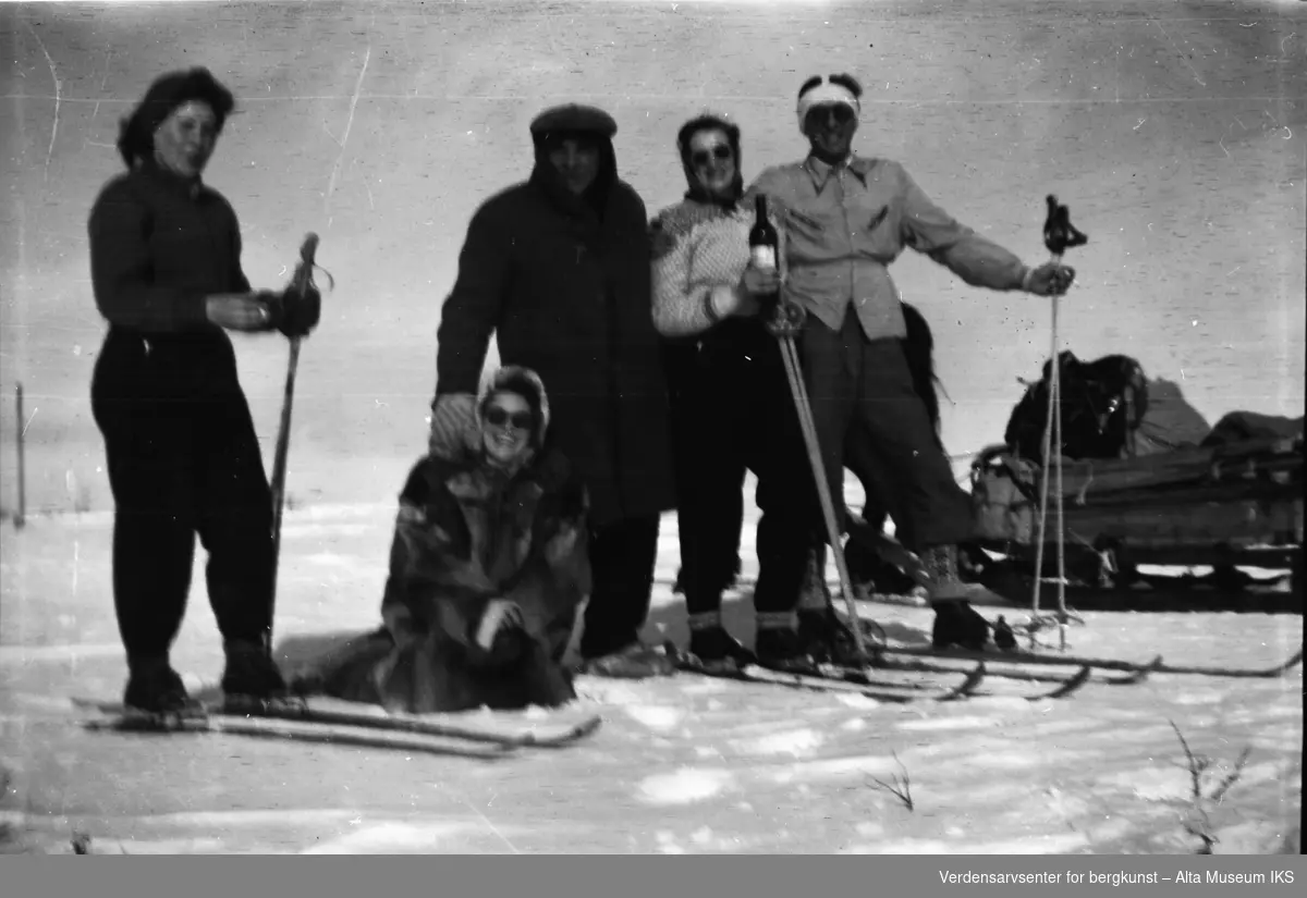 Fem venner smiler til kameraet. Solen skinner, og hesten Jacob står i bakgrunnen med en slede på slep. Tre av vennene er iført ski, og den ene holder en flaske vin. Erna Jøraholmen, iført pels, sitter på knærne i snøen.