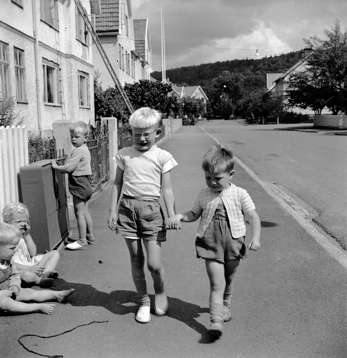 På en trottoar i Huskvarna sitter Lena Andersson, Per Andersson står vid elskåpet och Tom Andersson håller Leif Halldin i handen.