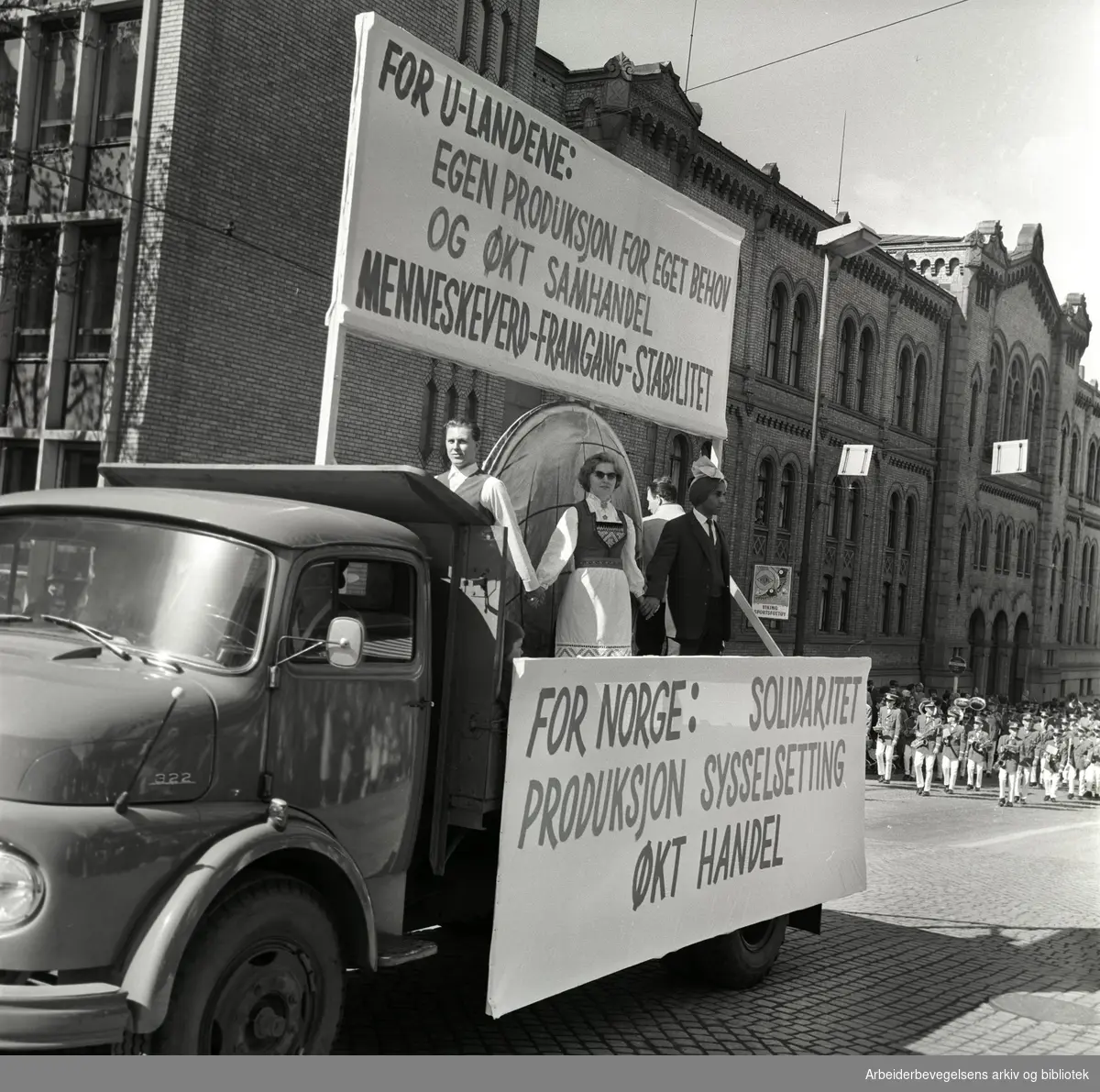 1. mai 1964 i Oslo.Demonstrasjonstoget i Karl Johans gate.Parole: For U-landene:.Egen produksjon for eget behov.og økt samhandel.menneskevern - framgang - stabilitet.Parole: For Norge: Solidaritet produksjon økt handel