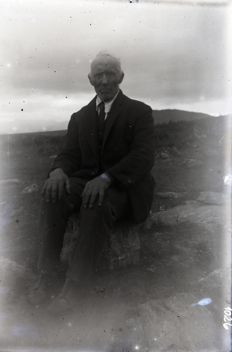 Bildet viser en dresskledd mann som sitter på en stein på fjellet. Han har lys skjorte og slips, og har klokke på armen.