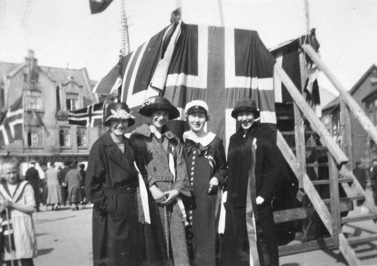 Unge kvinner foran flaggdekorert talerstol på Torvet. Bildet er tatt på 17. mai 1928. Rachel Strand med hvit lue.
