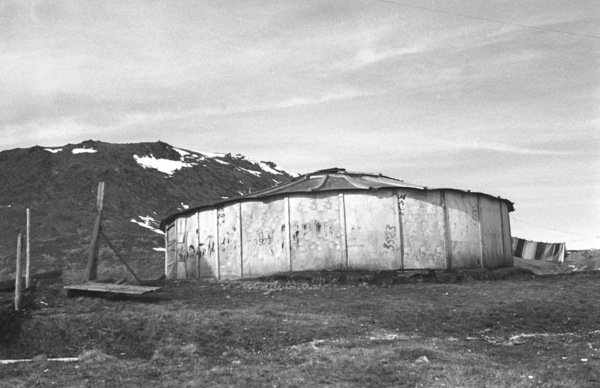 Tyske fangeboliger blev overtatt av hjemvendte Honningsvåginger, også de tyske fangers sykestue blev omgjørt til midlertidig bolig for hjemvendte. Dette bygget er sirkelformet. 

Arkitekt Ola Hanche-Olsen arbeidet ved Brente Steders Reguleringskontor i 1946. Hovedadministrasjon for gjenreisning av Nord-Troms og Finnmark ble lagt til Harstad og fikk navnet Finnmark kontoret. Landsdelen Nord-Troms og Finnmark blev oppdelt i syv distrikt med hver sin administrasjon. Honningsvåg, distrikt IV, skulle betjene Nordkapp, Lebesby, Porsanger og Karasjok kommune.

Ola Hanche-Olsen har tatt bildene. Han var født 13. mars 1920 i Borre, død 11. februar 1998 i Gjettum. Han hadde artium fra 1939, arkitekteksamen fra NTH 1946 og arbeidet deretter ved Finnmarkskontoret 1946–48 før han etablerte egen arkitektpraksis. Han debuterte som barnebokforfatter i 1974 med lettlest-boka "Knut og sjørøverne", og skrev i alt 12 bøker. 

Han var XU-agent 1944-45, og var også en aktiv fjellklatrer og friluftsmann. XU var den største og viktigste allierte etterretningsorganisasjonen i det okkuperte Norge under andre verdenskrig. Det meste av XUs virksomhet ble holdt hemmelig til 1988. Ola var gift med Solveig Hanche-Olsen (f. Falkenberg); de fikk 3 barn, blant dem matematikeren Harald Hanche-Olsen. 

