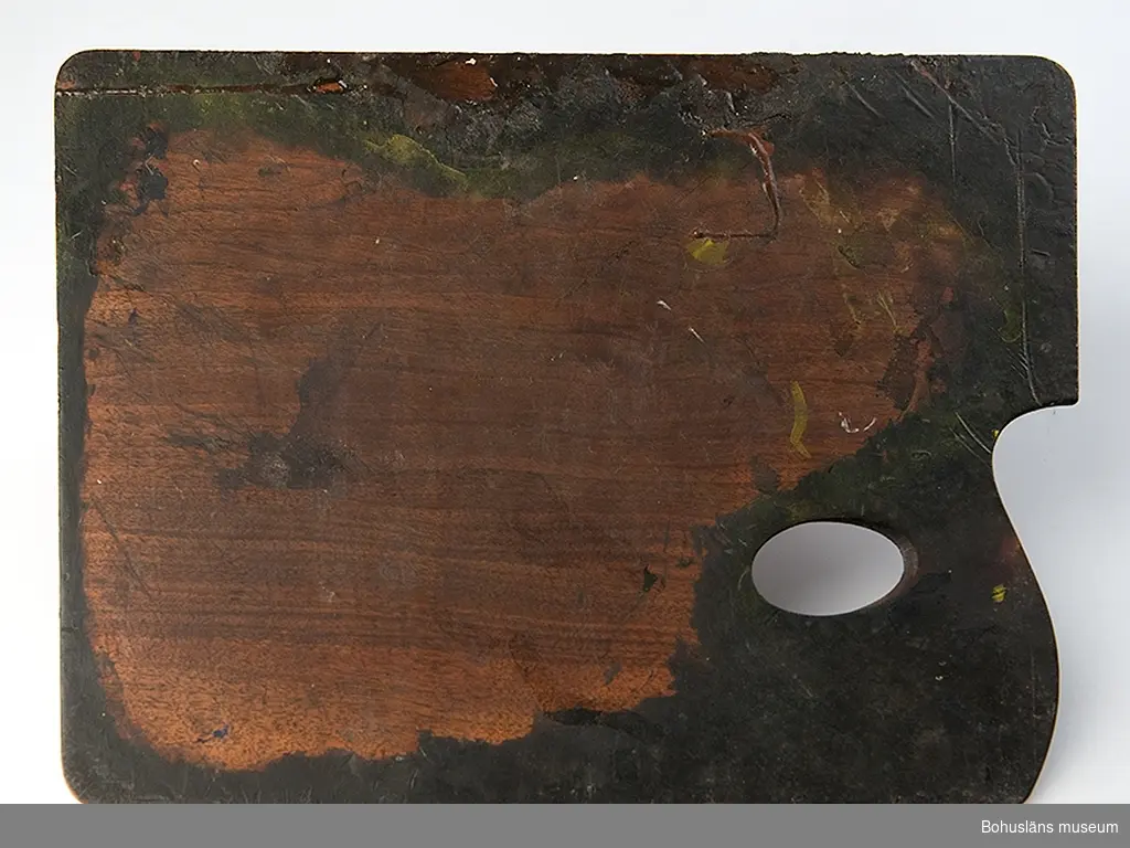Rektangulär palett av mahognyplywood med inhak i ena kortänden med plats för handlov och med hål för tumme.
retser av fernissa, svart tusch och oljefärg