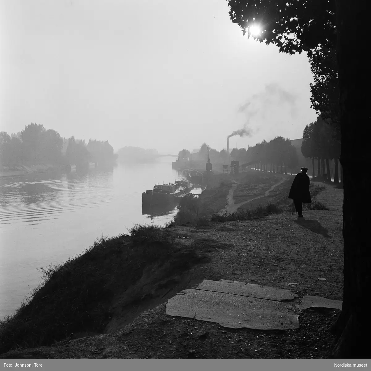 Paris. En man promenerar längs Seine (?). I bakgrunden flodpråmar förtöjda vid stranden.