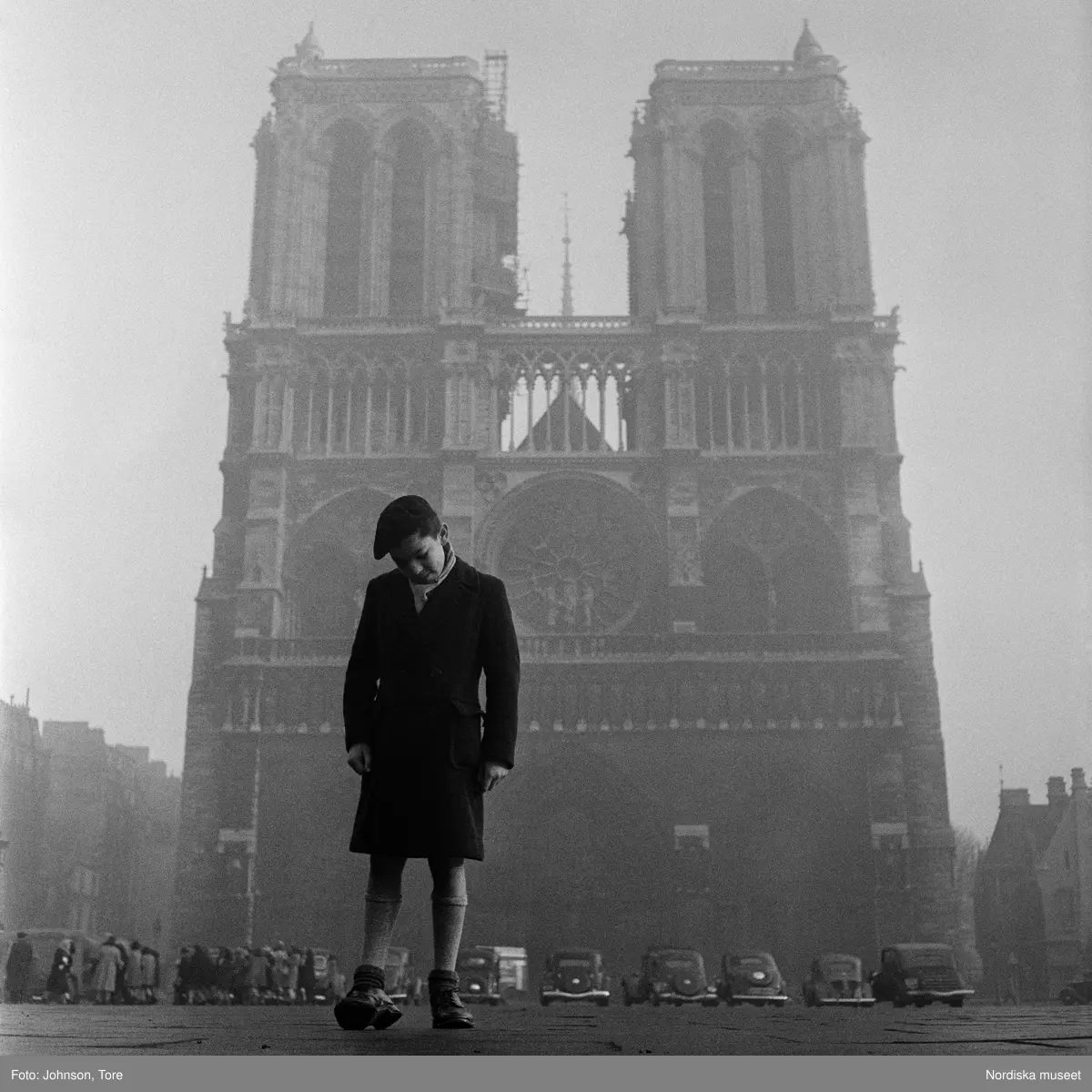 Paris. En pojke tittar ned i marken, Nôtre Dame i bakgrunden.