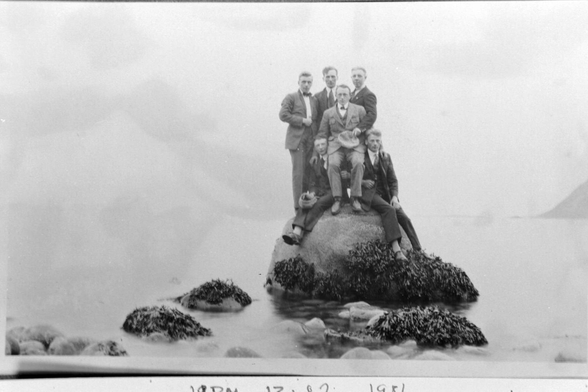 Seks menn på en stor stein i fjæra på Nupen.