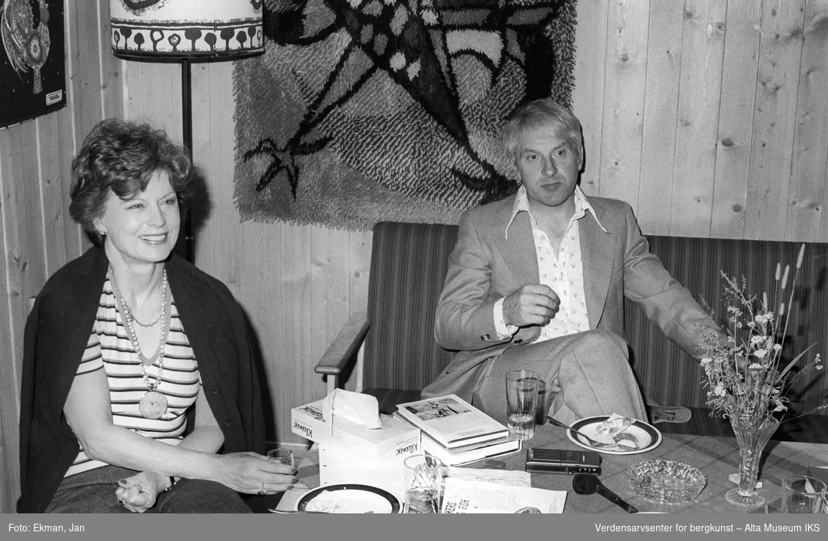 Hytteinteriør med personer.

Fotografert mellom 1970 og 1988.

Fotoserie: Laksefiske i Altaelva i perioden 1970-1988 (av Jan Ekman).
